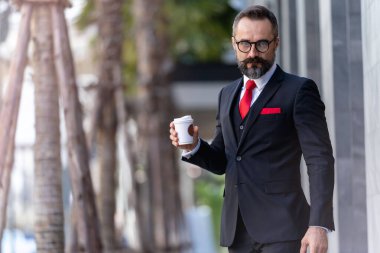 Takım elbiseli bir adam elinde kahve tutuyor. Sabahın köründe kahve saatinde iş hayatı. Taze ve mutlu hisseden adam, başarısından emin..