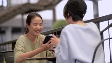 Güzel, genç Asyalı kadınlar alışveriş merkezinin kafesinde birlikte vakit geçiriyorlar ve aletler kullanıyorlar.