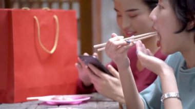 Güzel genç Asyalı kadınlar alışveriş yaparken birlikte sokak yemeği yiyorlar.