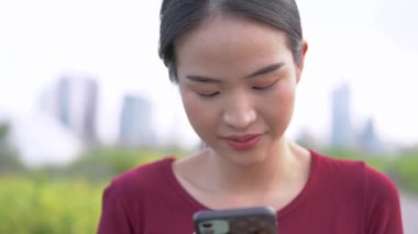 Açık havada akıllı telefon kullanan Asyalı genç bir kadının yakın çekim görüntüleri.