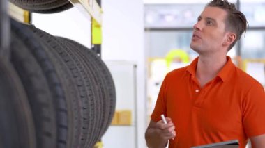 Otomobil servisi çalışanı, kapalı ambardaki tablet cihazıyla lastik stoklarını kontrol ediyor. Yedek parça taşımacılığının endüstriyel deposunda çalışan insanları düşünün.