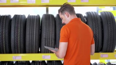 Otomobil servisi çalışanı, kapalı ambardaki tablet cihazıyla lastik stoklarını kontrol ediyor. Yedek parça taşımacılığının endüstriyel deposunda çalışan insanları düşünün.