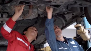 Fabrika elbiseli işçi ve kıdemli personel bir araba motorunun altını tamir ediyor ve kontrol ediyor bir garaj vagonunun otoparkını. Yedek parça taşımacılığının endüstriyel deposunda çalışanlar.