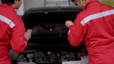 Fabrika elbiseli işçiler ön vagonu açıyor ve bir araba motorunu tamir ediyor bir garaj arabasını park ediyor. Yedek parça taşımacılığının endüstriyel deposunda çalışanlar.