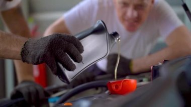 El işçiliği araba tamirini kapatın ve garaj otoparkındaki motora motor yağı ekleyin. Yedek parça taşımacılığının endüstriyel deposunda çalışanlar.