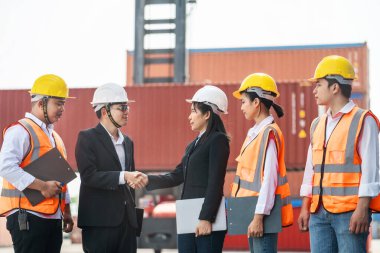 Erkek kadın mühendislerin ve işçilerin portresi konteynır ve kargo alanının önünde el sıkışıyor ve buluşuyorlar. Nakliye sektöründe çalışan kendinden emin ve zeki iş adamları..