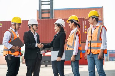 Erkek kadın mühendislerin ve işçilerin portresi konteynır ve kargo alanının önünde el sıkışıyor ve buluşuyorlar. Nakliye sektöründe çalışan kendinden emin ve zeki iş adamları..
