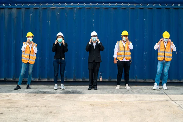 group people worker is wearing protection mask face and safety helmet and wearing suit safety dress With background cargo warehouse. industry worker operating. people have a social distancing space.