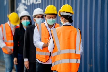 Yüz maskesi ve güvenlik elbisesi giyen fabrika işçisi, temassız kızılötesi termometreyle kuyrukta bekleyen işçilerde sıcaklık ölçümü kullandı