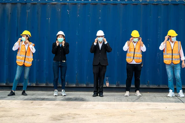 group people worker is wearing protection mask face and safety helmet and wearing suit safety dress With background cargo warehouse. industry worker operating. people have a social distancing space.