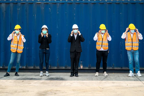 group people worker is wearing protection mask face and safety helmet and wearing suit safety dress With background cargo warehouse. industry worker operating. people have a social distancing space.
