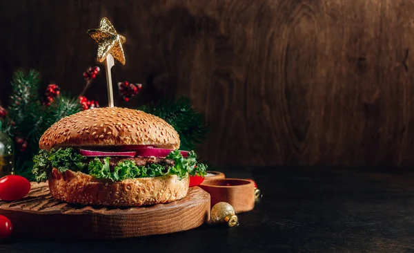 Homemade burger with black angus beef meat and fresh vegetables on a wooden board with Christmas decoration. Selective focus with copy space