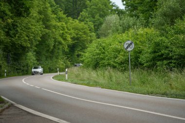 Kıvrımlı yol hız limiti tabelasının sonunda. Ağaçların arasındaki yol, 70 km / saat sınırının sonu, kavşağa yaklaşan arabalar..