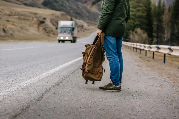 Hombre con una mochila en sus manos de pie en el borde del camino — Foto de Stock