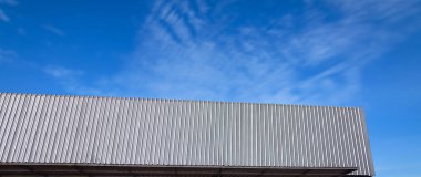 Mavi gökyüzünde metal katman çatı eğrisi. Modern inşaat, metal tırtıklı kemer açıklığı çatı kaplaması, büyük bina çatısı.