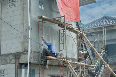 Arkasında çatı olan bir inşaat işçisi.
