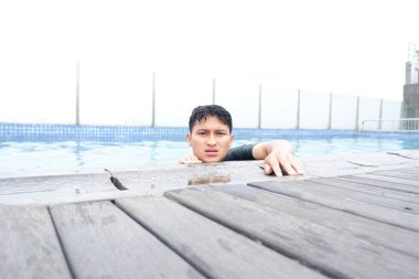 Yüzme havuzunda oturan Asyalı genç adamın portresi