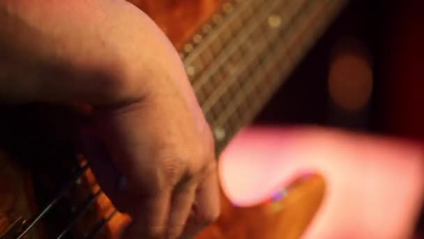 暗い背景、ジャズ音楽、ベースギター、エネルギッシュなギター、美しい男の手をピンクのシャツのミュージシャンのギターを弾きギター チェリー色 — ストック動画