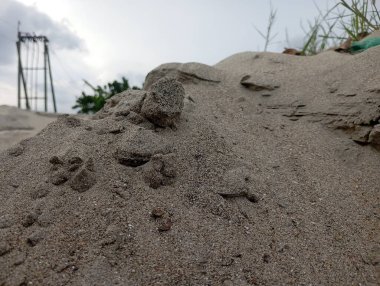 Endüstriyel yapısı ve yeşilliği olan bulutlu gökyüzüne karşı engebeli kum yığınlarını kapatın