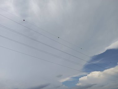 Uzak kırmızı işaretler, gökyüzünde dramatik bulutlar ve mavi noktalarla güç hatlarına rehberlik eder.