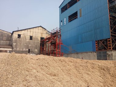 Büyük mavi ve gri binalar ve odun parçalarıyla sanayi bölgesi