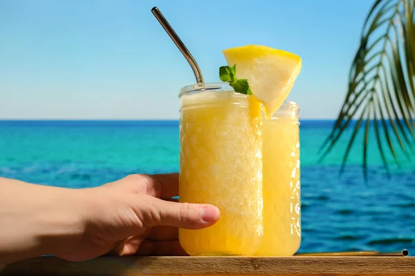 Hand with melon smoothie, blue sea on background.