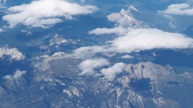 Karlı tepeleri ve mavi gökyüzünde bulutları olan havadaki dağ manzarası. Geniş, sakin doğa manzarası.