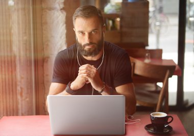 Genç Sakallı İş Adamı Siyah Tişört Giyiyor Laptop Şehir Kafesi 'nde çalışıyor. Oturan Ahşap Masa Kahvesi Müziği Dinliyor. Çalışma Süreci Başlıyor. Bulanık Özgeçmiş..