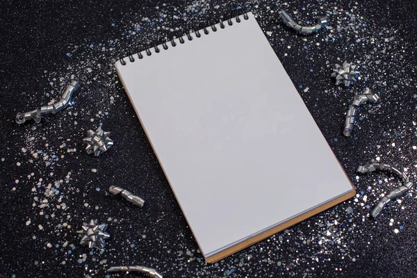 Confeti y cuaderno. Lista de objetivos de resolución de año nuevo con estrellas de brillo plateadas sobre fondo negro. — Foto de Stock