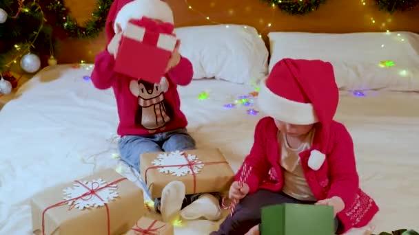 Duas meninas bonitos irmãs abrindo presentes de Natal no quarto da cama — Vídeo de Stock