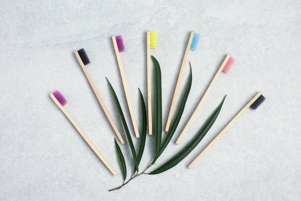 Bamboo toothbrushes and green leafs on stone table