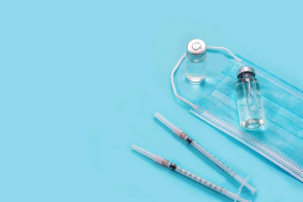 Vaccini e siringhe, maschera viso su sfondo blu. — Foto Stock