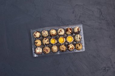 Siyah arka planda şeffaf plastik bir kabın içinde bıldırcın yumurtaları.