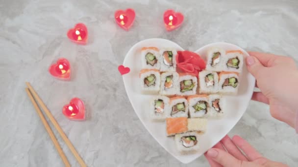 Les mains féminines mettent un plateau en forme de coeur avec Sushi mis dans une table. — Video