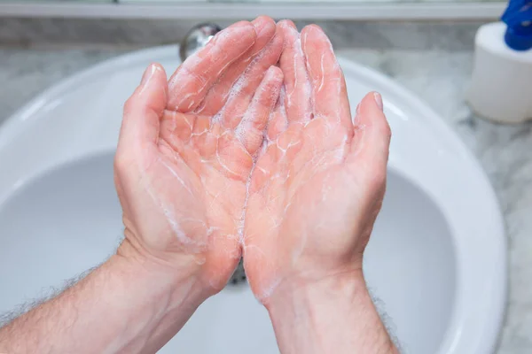 A Man is washing his hands with soap in bathroom.