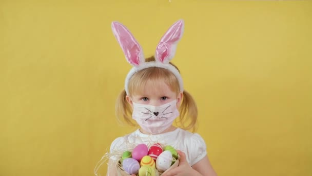 Schattig meisje met konijnenoren In een medisch masker toont paaseieren en toont uw glimlach zonder masker — Stockvideo