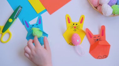 Çocuk elleri kağıttan bir tavşanın Paskalya yumurtasını yerleştirir..