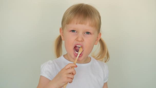 De près. Petite enfant blonde fille enfant riant et se brosse les dents avec diligence avec du dentifrice. — Video