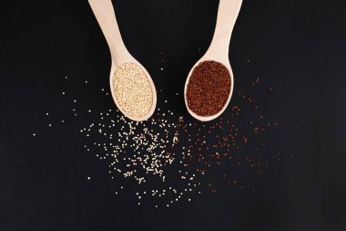 Çiğ organik kırmızı ve beyaz kinoa tanecikleri, siyah arka planda tahta kaşıklarda..