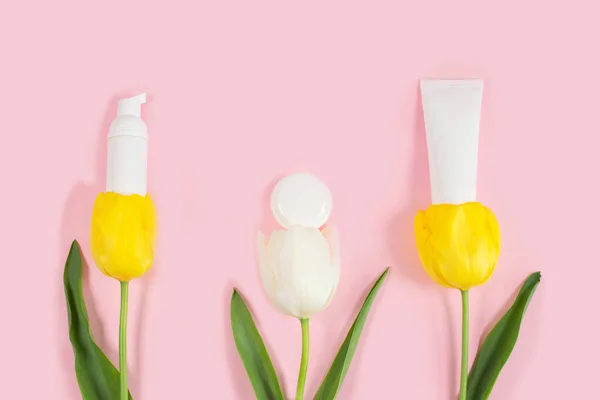 Botol kosmetik putih berisi bunga kuning dan tulip putih. — Stok Foto