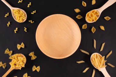 Tahta kaşıklarla farklı makarna türleri ve boş ahşap tabaklar.