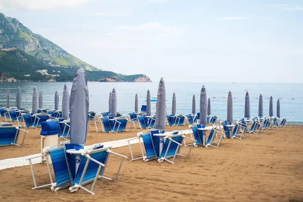 Empty white sun loungers without people under umbrellason the pebble beach by the sea. — Stock Photo, Image