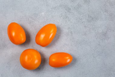 Açık gri zemin üzerinde taze sarı turuncu domatesler.