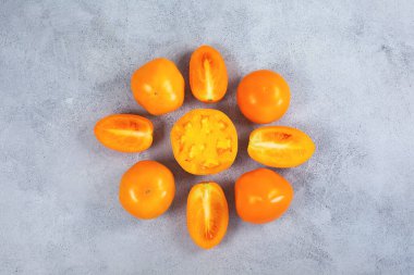 Açık gri zemin üzerinde taze sarı turuncu domatesler.