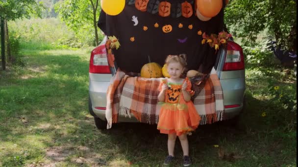 Little Kid menina Halloween, sentado no porta-malas do carro e comer doces de baldes. — Vídeo de Stock