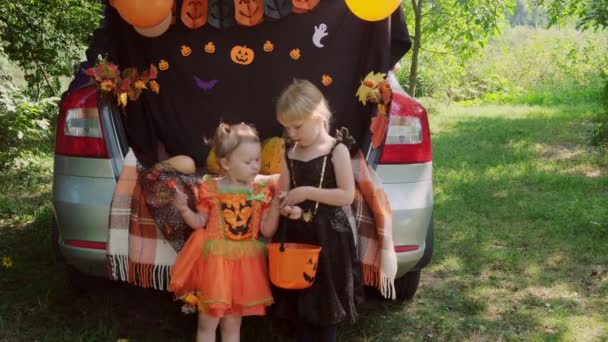 Two little sisters celebrating Halloween and eating candy from buckets sitting in trunk of car. — Stock Video