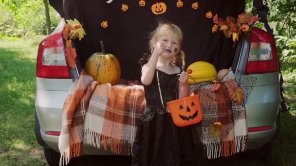 Bambina Halloween, seduta nel bagagliaio della macchina e che mangia caramelle dai secchi. — Video Stock