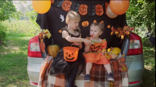 Dvě malé sestřičky slaví Halloween a jedí sladkosti z kbelíků sedících v kufru auta. — Stock video
