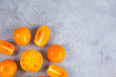 Açık gri zemin üzerinde taze sarı turuncu domatesler.