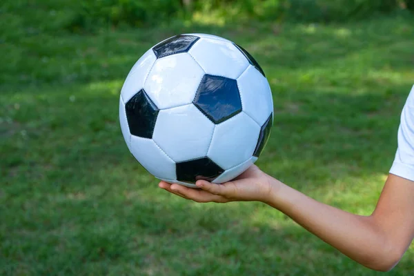 Fußball weißes und schwarzes Leder in der Hand eines Fußballers auf grünem Rasen. — Stockfoto